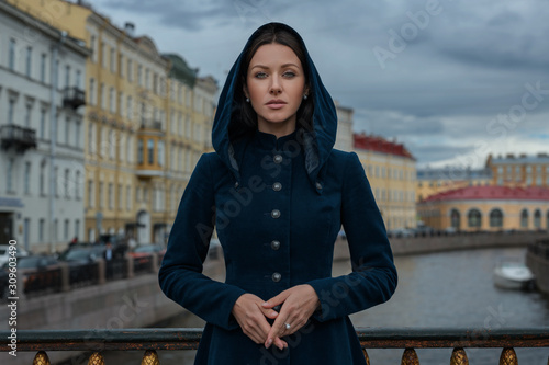 Poetic brown hair brunette sister beautiful woman girl vintage classic coat blue dress look camera green eyes hands together street old town outdoor blue sky river cars channel scenic city view