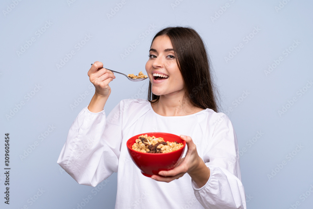 Young woman over isolated blue background holding a bowl of cereals
