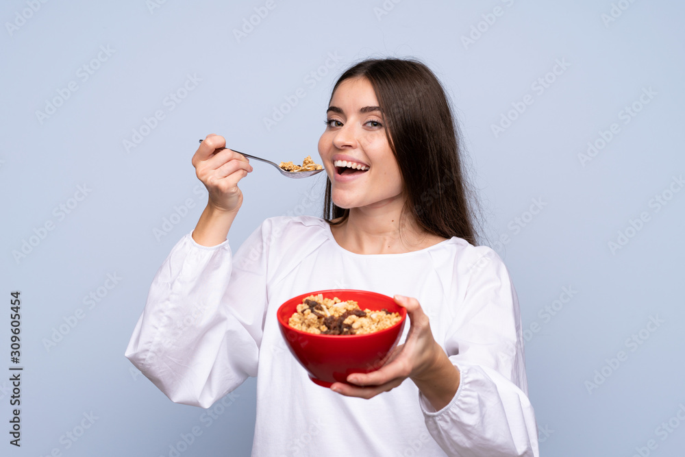 Young woman over isolated blue background holding a bowl of cereals Young woman over isolated blue background holding a bowl of cereals