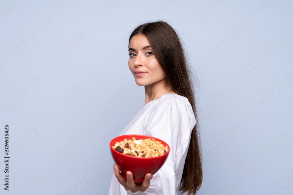 Young woman over isolated blue background holding a bowl of cereals Young woman over isolated blue background holding a bowl of cereals