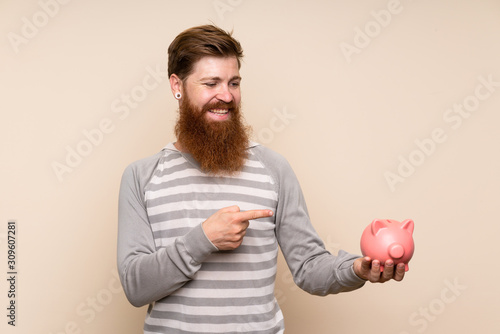 Redhead man with long beard over isolated background holding a big piggybank