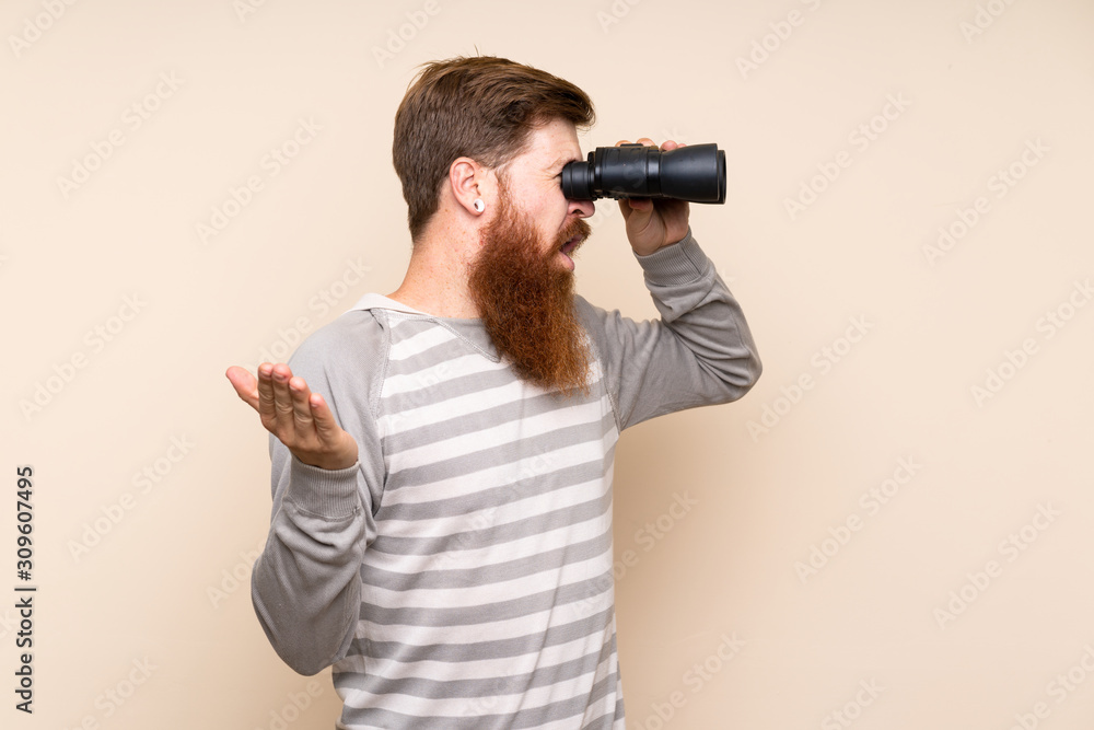 Redhead man with long beard over isolated background with black binoculars Redhead man with long beard over isolated background with black binoculars