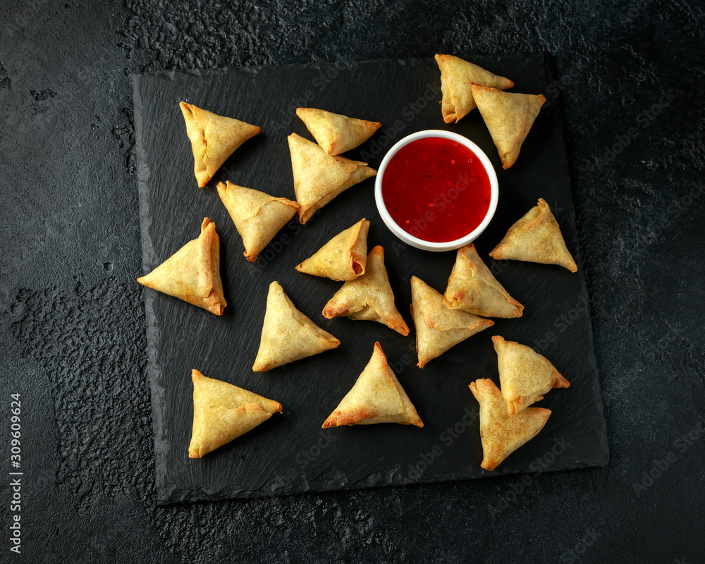 Fresh Indian Samosa with dipping sweet chili sauce on rustic stone board Fresh Indian Samosa with dipping sweet chili sauce on rustic stone board