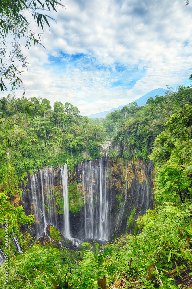 (High Dynamic Range image) Stunning aerial view of the Tumpak Sewu Waterfalls also known as Coban Sewu with clouds raising from the canyon. Semeru volcano in the distance.