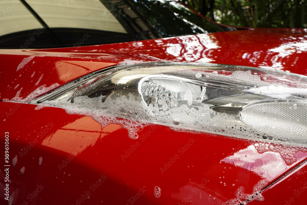 red wet car with bubble from car wash and wax shampoo at the headlight