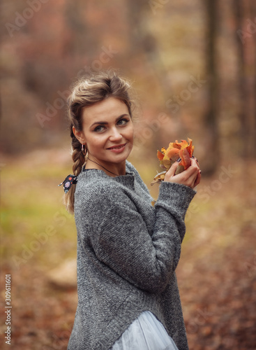 Attractive woman with braided pigtails holds fallen leaves in her hands in the autumn forest. Autumn art portrait