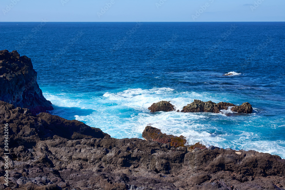 Deep blue water with waves, white foam and volcanic cliffs. Canary Islands. Lanzarote, volcanic island. The magnificent coast of the Atlantic Ocean.