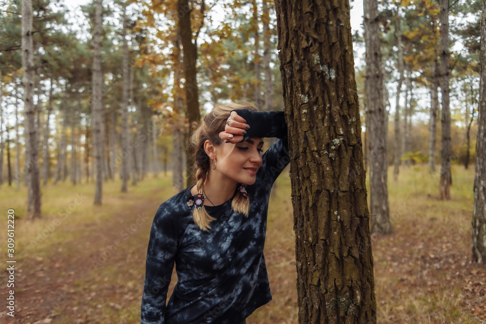 Young tired fit woman in sportswear leaned on a tree after an intense jog in the autumn forest. Healthy lifestyle concept. Outdoor workout