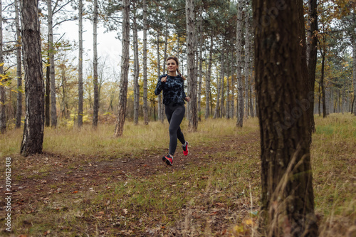 Jogging in the autumn forest. Young fit woman in sportswear runs along forest path. Healthy lifestyle concept