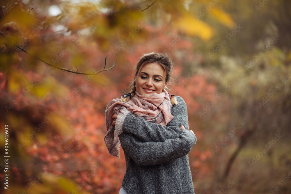 Art portrait. Young cheerful woman in autumn clothes posing in a forest with reddened leaves of trees