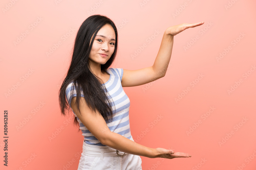 Teenager asian girl over isolated pink background holding copyspace to insert an ad Teenager asian girl over isolated pink background holding copyspace to insert an ad