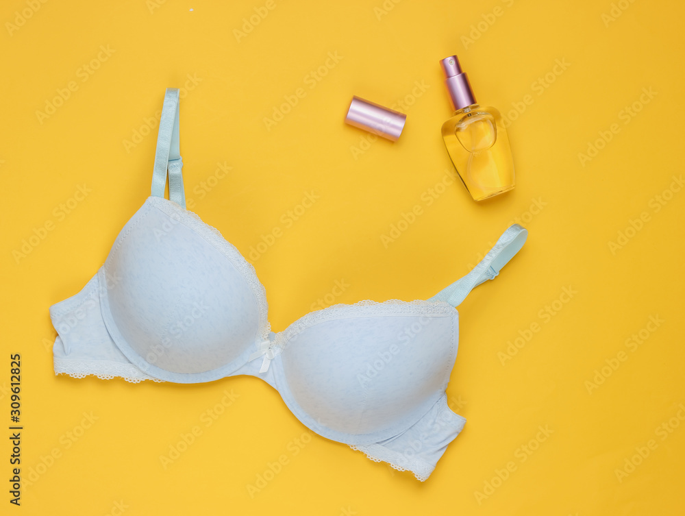 Stylish bra, perfume bottle on yellow pastel background. Top view. Beauty and fashion minimalistic still life Stylish bra, perfume bottle on yellow pastel background. Top view. Beauty and fashion minimalistic still life