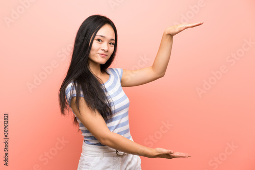 Teenager asian girl over isolated pink background holding copyspace to insert an ad © luismolinero