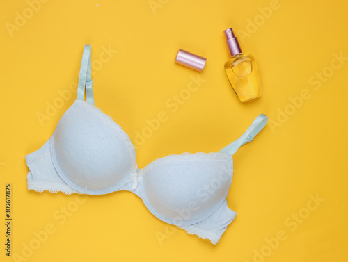 Stylish bra, perfume bottle on yellow pastel background. Top view. Beauty and fashion minimalistic still life