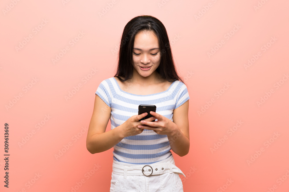 Teenager asian girl over isolated pink background sending a message with the mobile Teenager asian girl over isolated pink background sending a message with the mobile