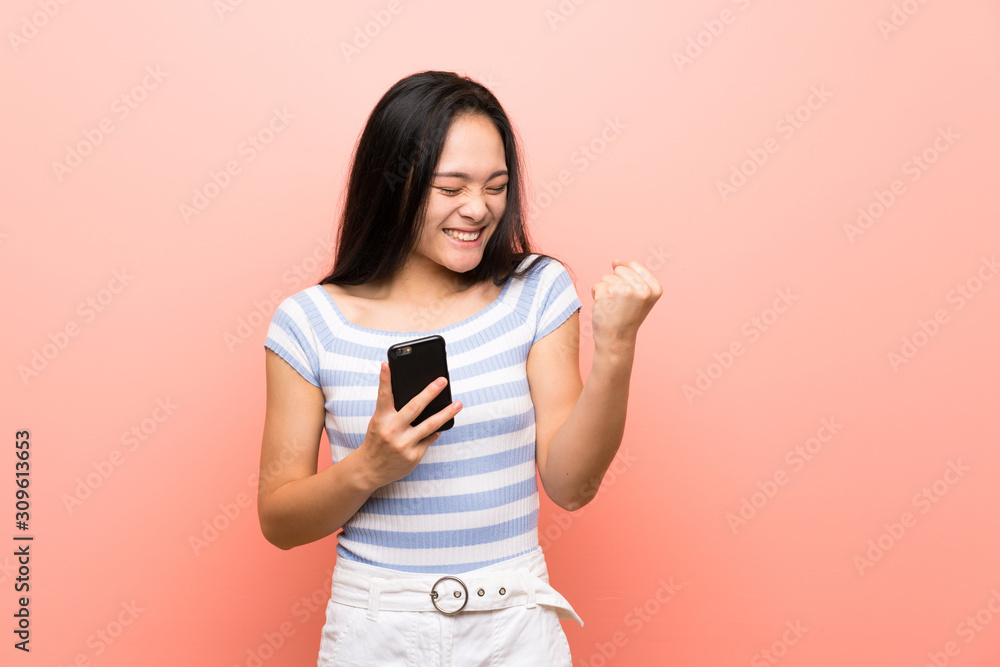 Teenager asian girl over isolated pink background with phone in victory position Teenager asian girl over isolated pink background with phone in victory position
