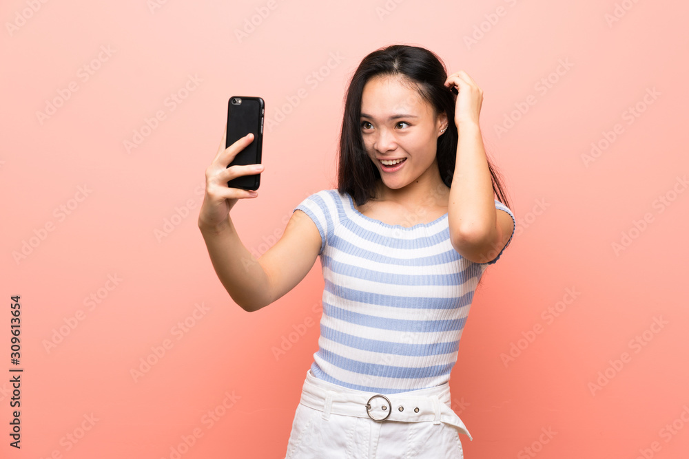 Teenager asian girl over isolated pink background making a selfie