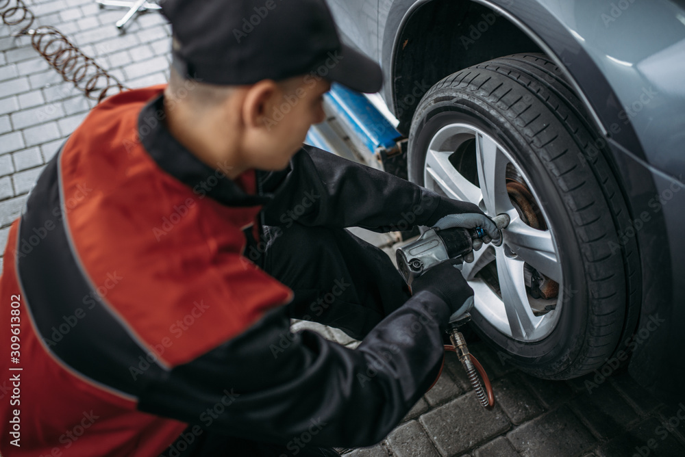 Mechanic with pneumatic wrench unscrews the wheel Mechanic with pneumatic wrench unscrews the wheel