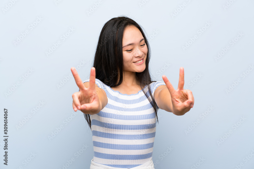 Teenager asian girl over isolated blue background smiling and showing victory sign Teenager asian girl over isolated blue background smiling and showing victory sign