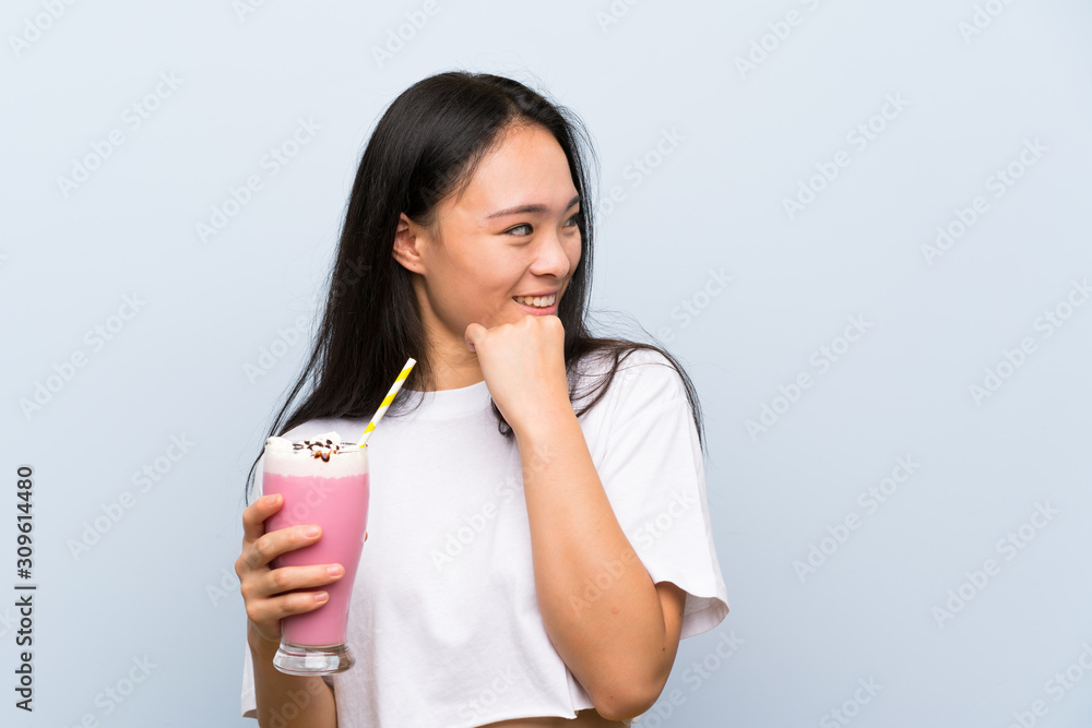 Teenager asian girl holding a strawberry milkshake thinking an idea and looking side Teenager asian girl holding a strawberry milkshake thinking an idea and looking side