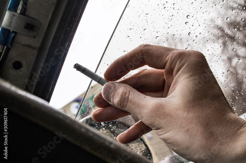 hand Smoking driver close up with a cigarette in a slightly open car window during the rain