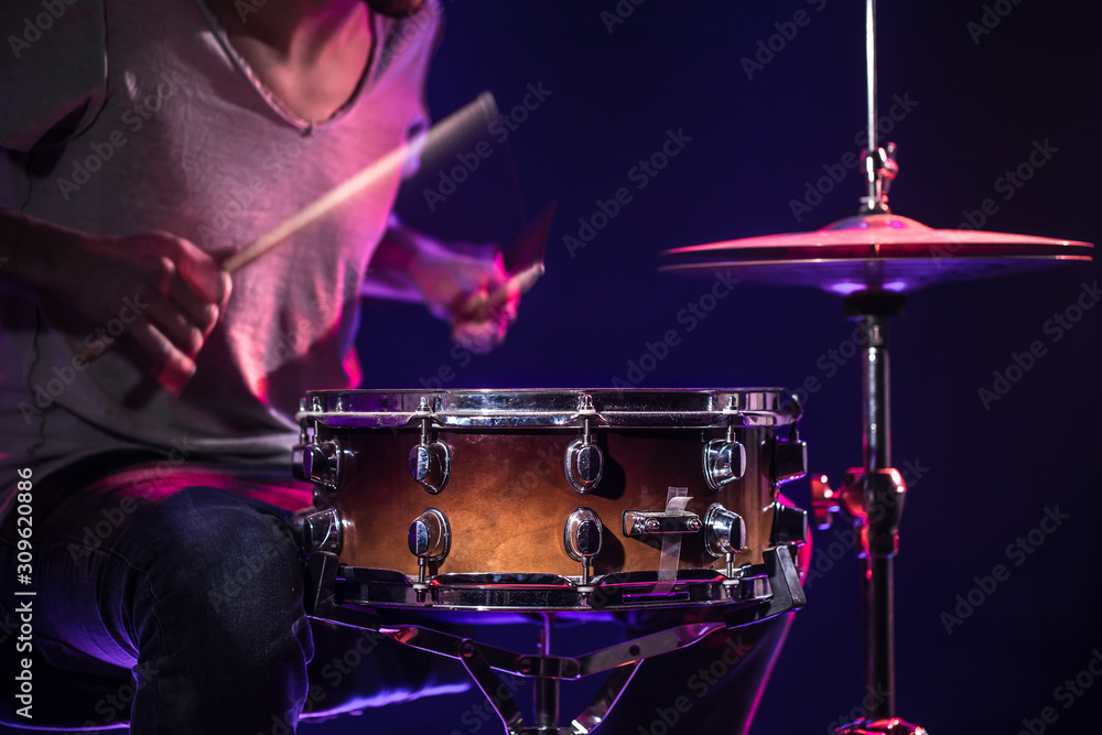 Naklejka premium The drummer plays the drums. Beautiful blue and red background, with rays of light. Beautiful special effects smoke and lighting. The process of playing a musical instrument. Close-up photo.