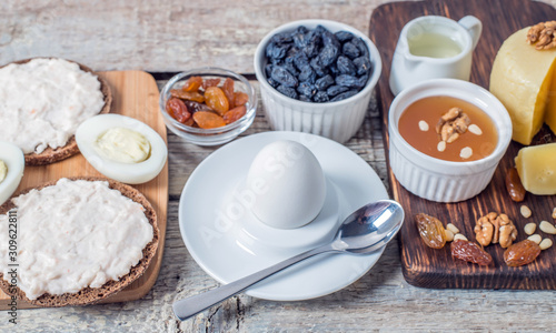 Boiled egg in egg cup and sandwich with cheese with slice egg, raisin, honey, parmesan, nut and pumpkin seed. Healthy breakfast on a wooden table