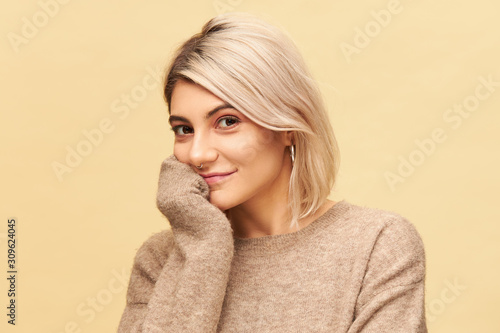 Isolated shot of adorable young European female with dyed bob hairstyle looking at camera with curious joyful smile, holding hand under chin, listening attentively. People and lifestyle concept © Anatoliy Karlyuk