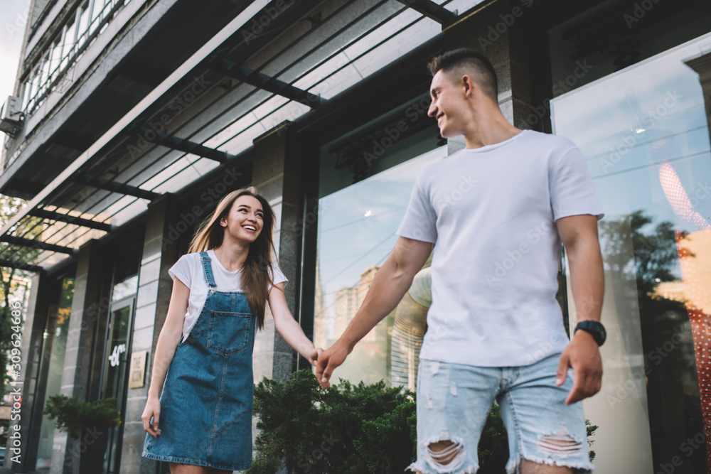 Cheerful couple in love rejoicing during journey travel for exploring new city and urban setting, positive Caucasian man and woman in trendy wear walking during date for flirting at urban setting