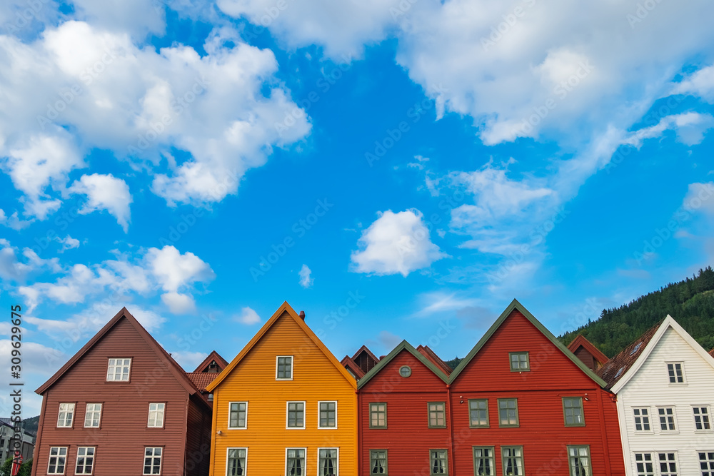 Historical white, red, brown, and yellow buildings in Bryggen - Hanseatic wharf in Bergen, Norway. Scenic summer panoramic view of the Old Town pier architecture under cloudy blue sky Historical white, red, brown, and yellow buildings in Bryggen - Hanseatic wharf in Bergen, Norway. Scenic summer panoramic view of the Old Town pier architecture under cloudy blue sky