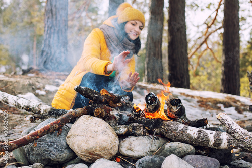 Woman young adult happy warms her hands by the fire on the background of a beautiful winter landscape in nature
