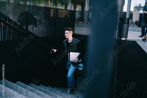 Modern man with laptop walking upstairs on street