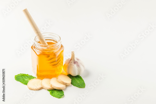 Glass jar of honey and dipper with ginger, mint, carnation, cinnamon and lemon isolated on a white background with space for text 