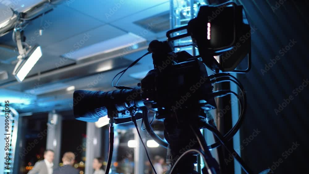 Professional camera with external monitor and commutation equipment stands on a tripod in a news studio. TV camera for broadcasting or media production works live.
