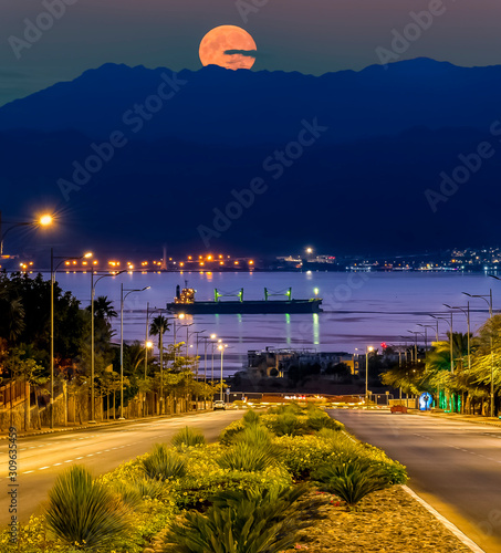 Moon rise above the Jordanian mountains, below is the gulf of Aqaba with anch...