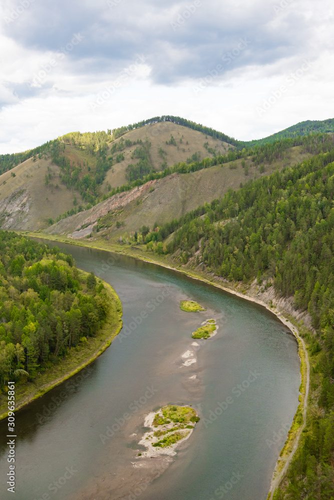 Fototapeta premium wide river among green hills with trees, smooth bend of channel, forest on shore of reservoir, summer swimming and navigation