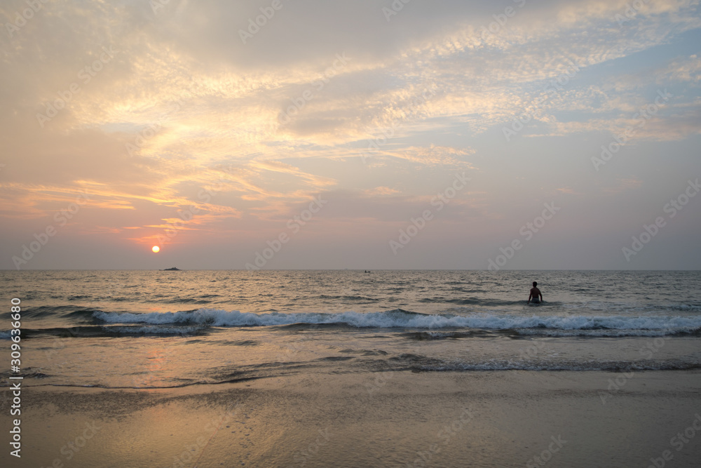 Beautiful sunset in indian Kudle beach of Gokarna, person swimming in the waves, Karnataka state.
