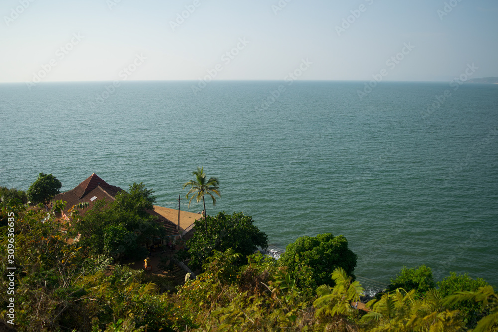 High view tropic sea landscape with green trees, palms and houses with tile roof at gokarna beach in India.