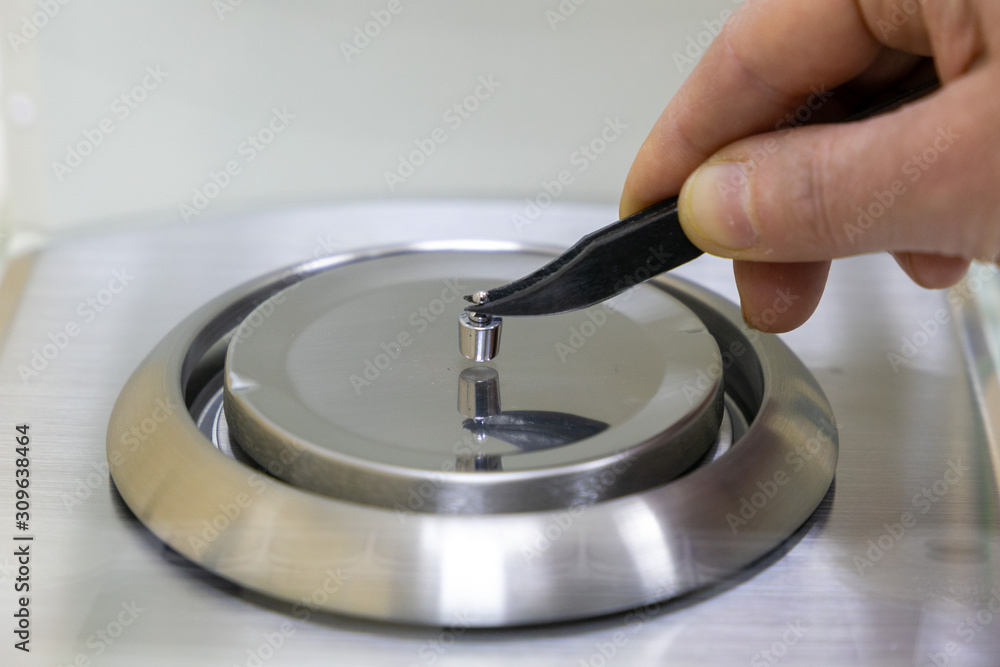 A scientist (doctor or pharmacist) weighs a small metal object on an accurate analytical balance. A scientist (doctor or pharmacist) weighs a small metal object on an accurate analytical balance.