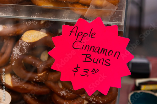A close up view of a colorful red price sign for freshly prepared apple cinnamon buns on a market stall during a local street fair, with copy space