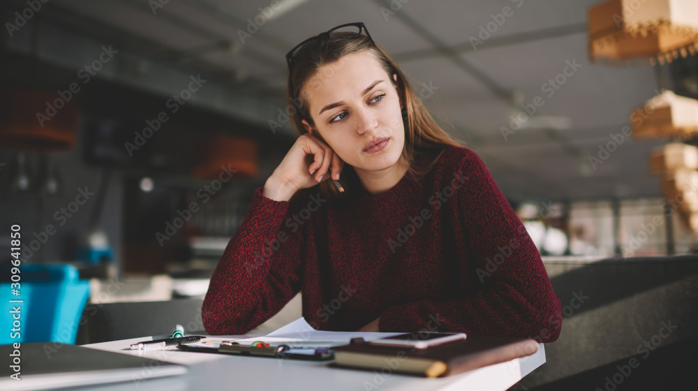 Young caucasian woman 20 years old thoughtfully looking aside while sitting in cozy cafe, attractive skilled hipster girl dreaming about future travel trip with friends during drawing sketches Young caucasian woman 20 years old thoughtfully looking aside while sitting in cozy cafe, attractive skilled hipster girl dreaming about future travel trip with friends during drawing sketches