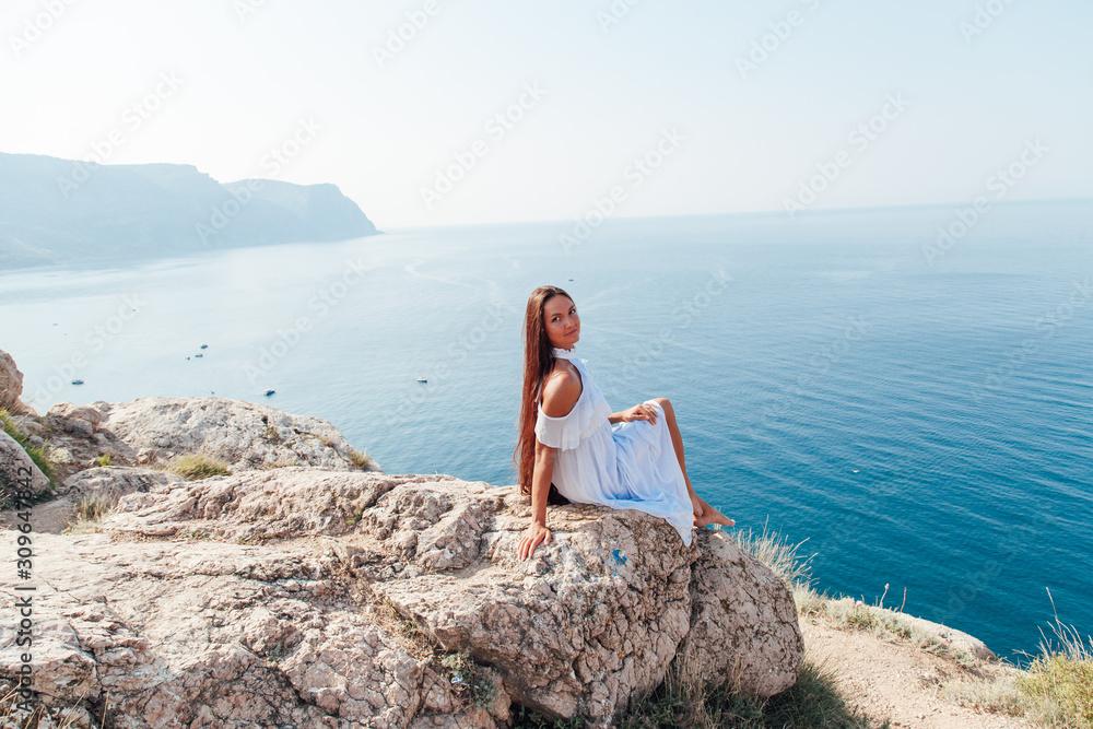 Beautiful woman with long hair in dress on cliff landscape in a journey