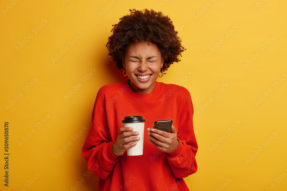 Portrait of overjoyed African American woman makes notes in smartphone, being in high spirit, holds paper cup with drink, dressed casually, makes shopping online, browses internet, isolated on yellow Portrait of overjoyed African American woman makes notes in smartphone, being in high spirit, holds paper cup with drink, dressed casually, makes shopping online, browses internet, isolated on yellow