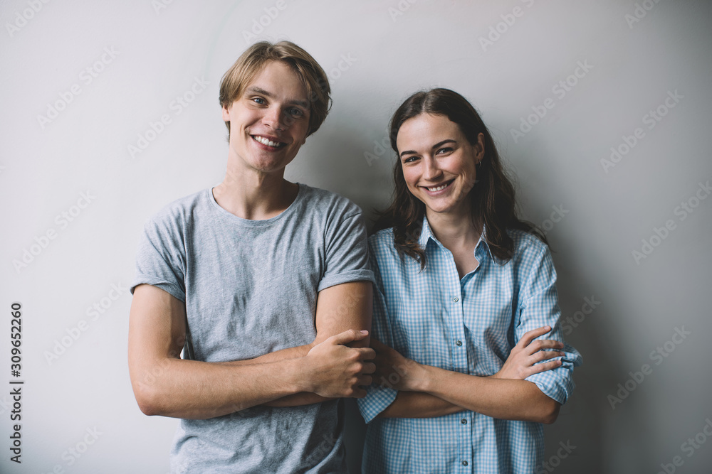 Half length portrait of cheerful male and female friends standing at publicity area with crossed hands and smiling at camera on leisure, successful man and woman in joyful mood laughing indoors Half length portrait of cheerful male and female friends standing at publicity area with crossed hands and smiling at camera on leisure, successful man and woman in joyful mood laughing indoors