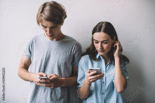 Millennial hipster guys dressed in casual wear holding cellular gadgets in hands ignoring live communication prefere smartphone chatting, Caucasian male and female bloggers networking websites photo