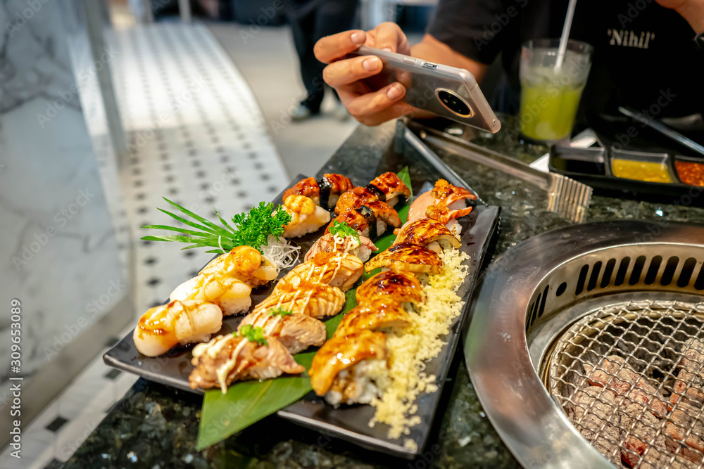 Bangkok Thailand, December 14, 2019. Man take a photo of Sushi set in japanese restaurant,Hotate (Scallop), shrimp,eel (Unagi),salmon burn,Ikura (Salmon egg), Foie gras.
