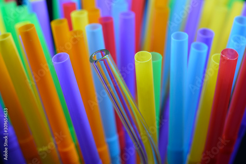 A reusable transparent glass straw among group of colorful plastic straw