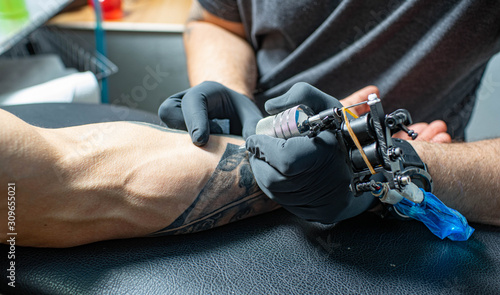 Male arm with tattoo. Master in black gloves is preparing to draw new tattoo. Tattoo machine.