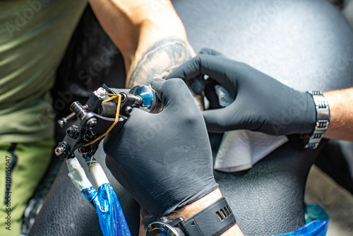 Tattoo salon. Master in sterile gloves draws black tattoo on male arm. Tattoo machine.