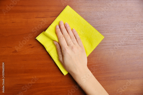 Hand cleans a wooden surface with a yellow napkin